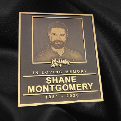 "In loving memory, Shane Montgomery 1981-2026" memorial plaque for Stingray Cheerleading