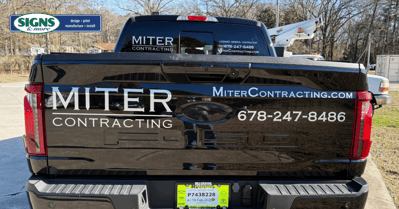 Rear view of a black pickup truck with Miter Contracting fleet decals on the tailgate, including the company website and phone number.