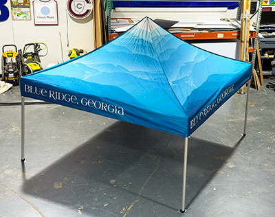 Custom printed pop-up canopy tent featuring a Blue Ridge, Georgia mountain landscape with Blue Ridge, Georgia branding on the valance, displayed in the Signs and More production facility before delivery.